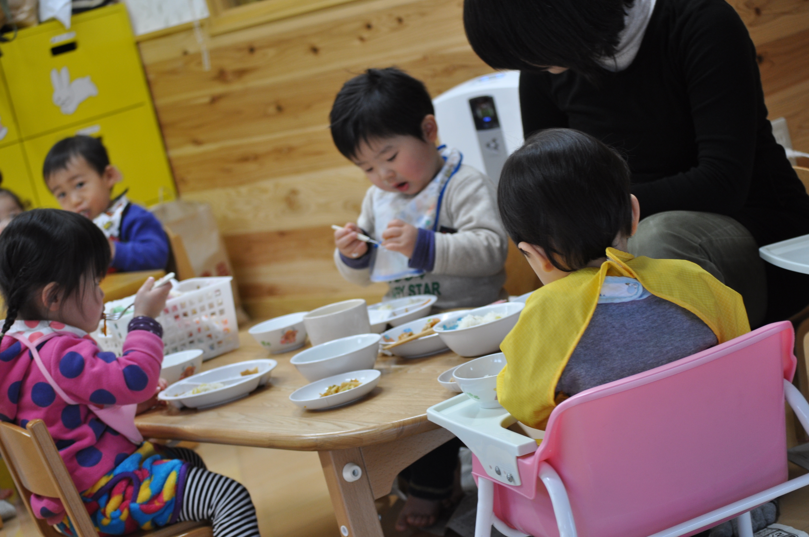 低い机を囲んで、スプーンを持って給食を食べる小さな子どもたち