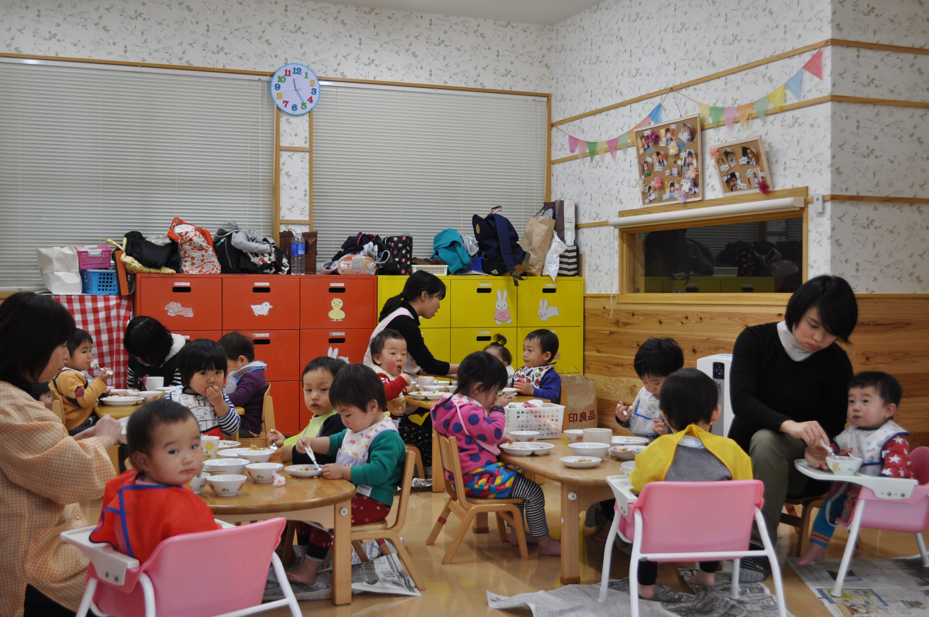 小さなテーブルにならんで座り、先生と一緒に給食を食べる未満児クラスの子どもたち