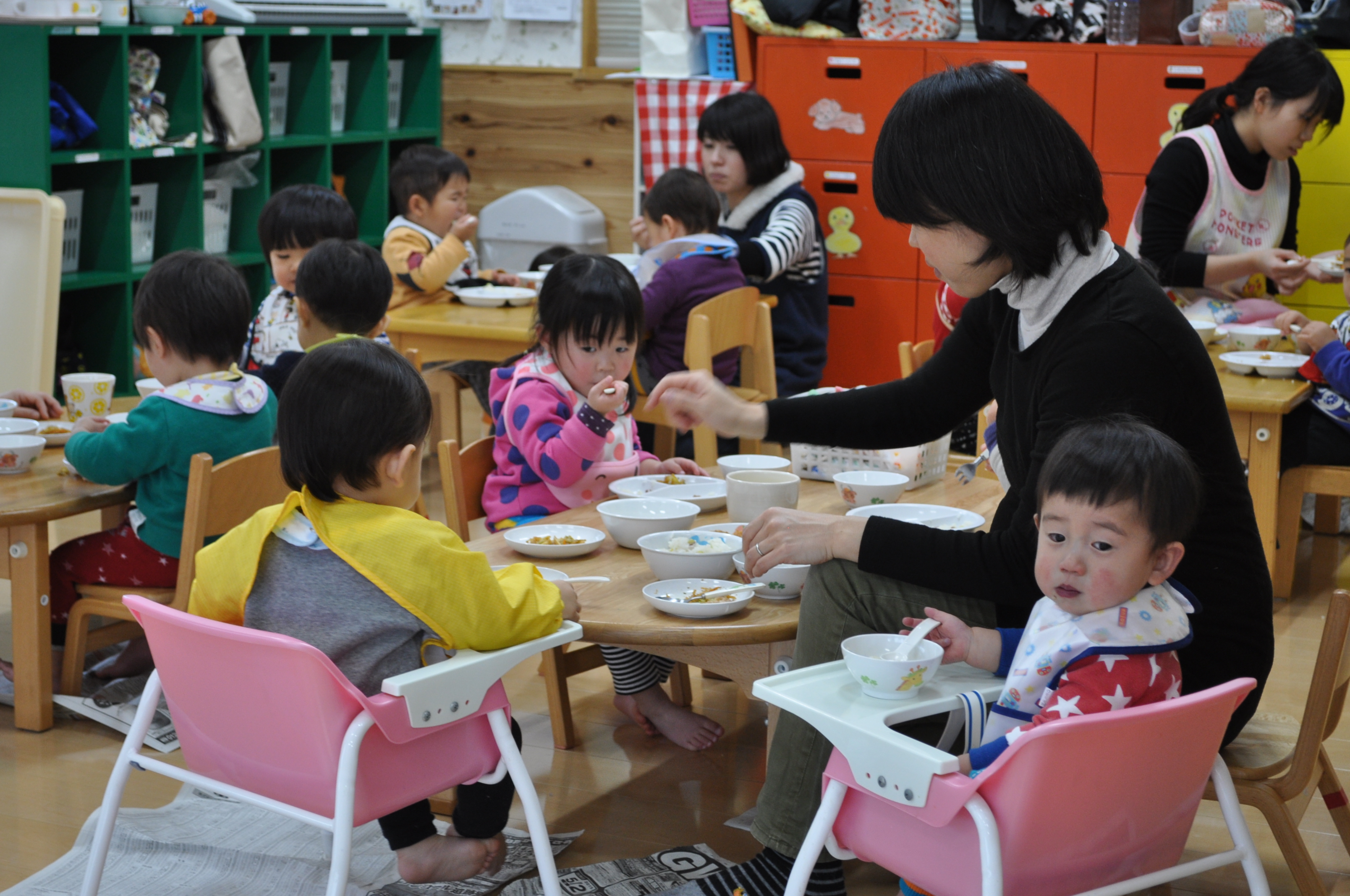 給食の時間、小さな子どものとなりに座って食事に付きそう先生