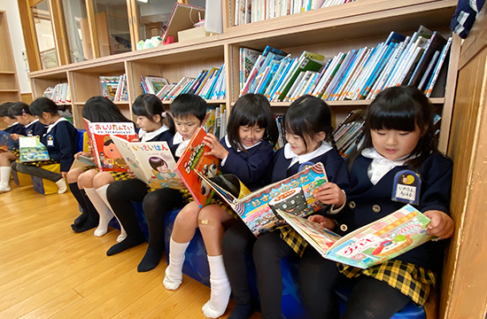 えほんの部屋で、本棚の前に座って絵本を読む子どもたち