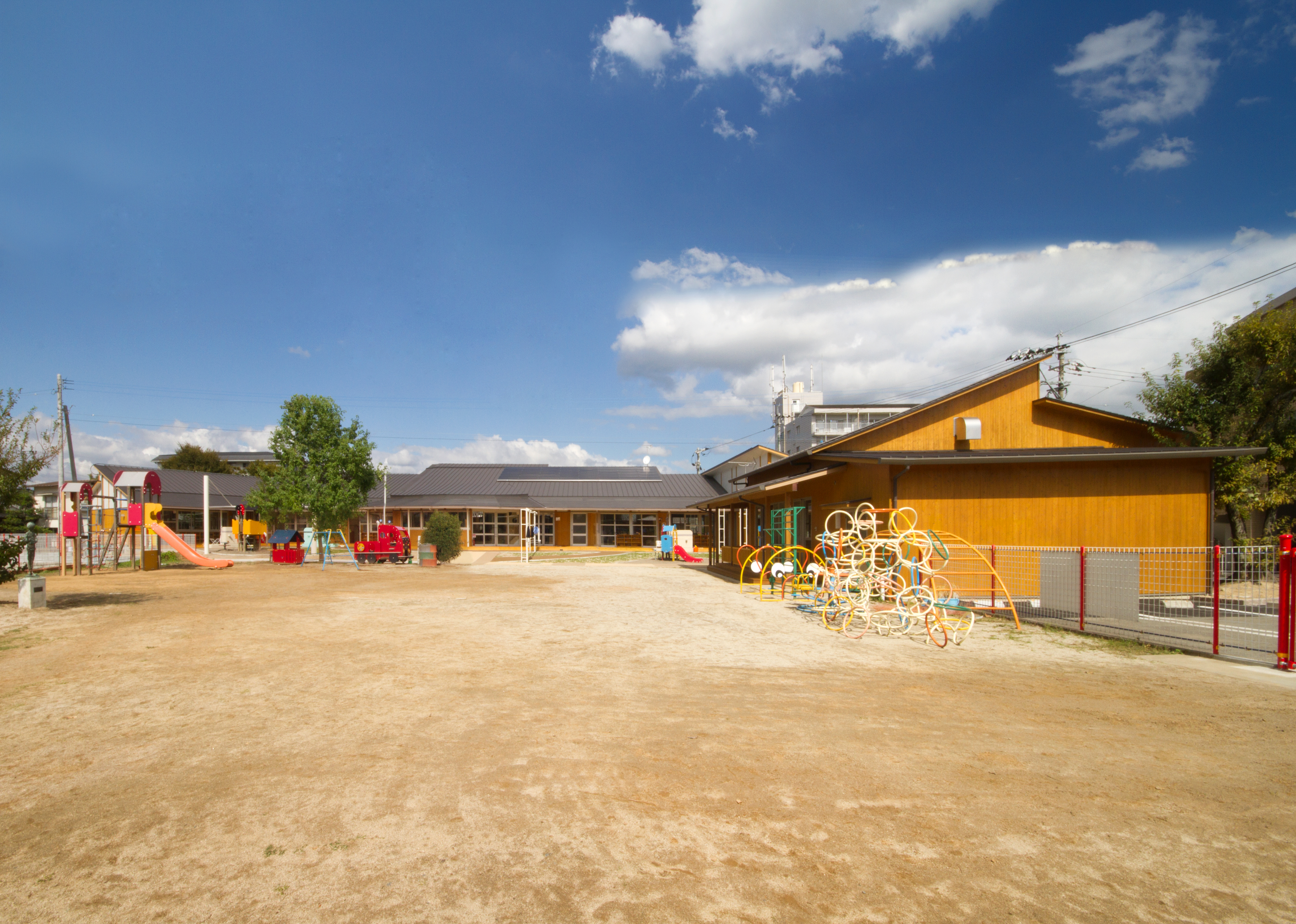 広い園庭のむこうに木造平屋の園舎がならび、右手に総合遊具が見える園庭の全景
