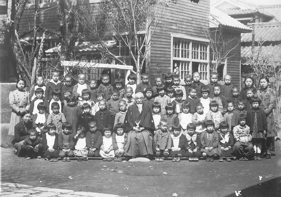 創立のころの記念写真。園舎の前に園児と職員が並んでいるモノクロ写真