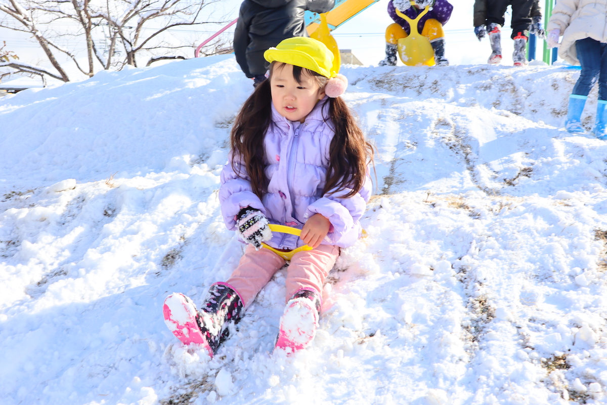 雪のつもった斜面に腰をおろして、そりすべりの順番を待つ子ども