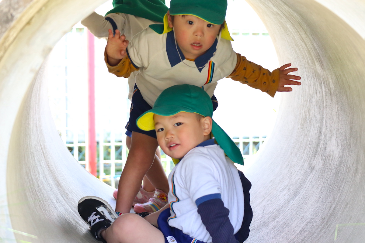 園庭のトンネル型の遊具の中から、こちらをのぞく二人の子ども