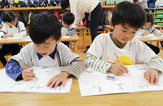 机に向かって、えんぴつでひらがなをなぞる二人の子ども