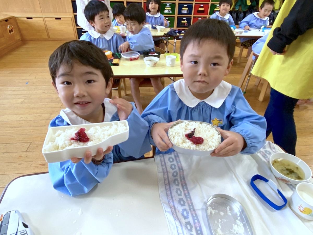 自分のごはんを手に持って、うれしそうにこちらへ見せる二人の子ども