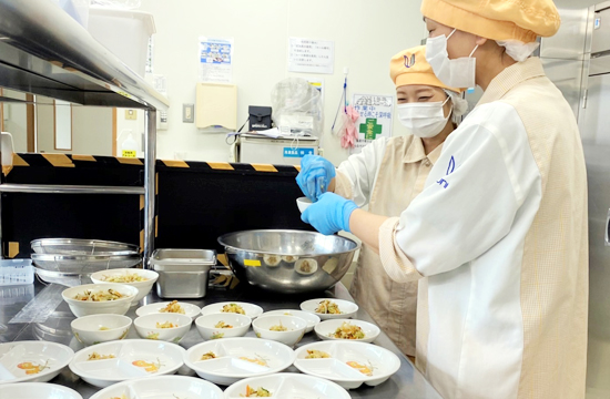 園内の給食室で、その日の給食を一人分ずつ盛りつける調理員