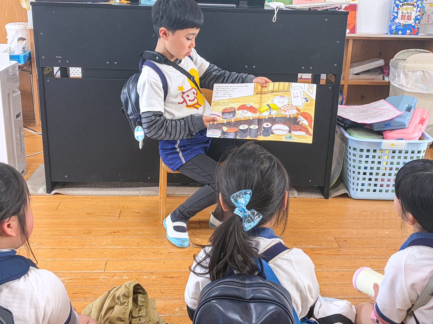 保育室で、友達に絵本を読む子どもと、耳をかたむける子どもたち