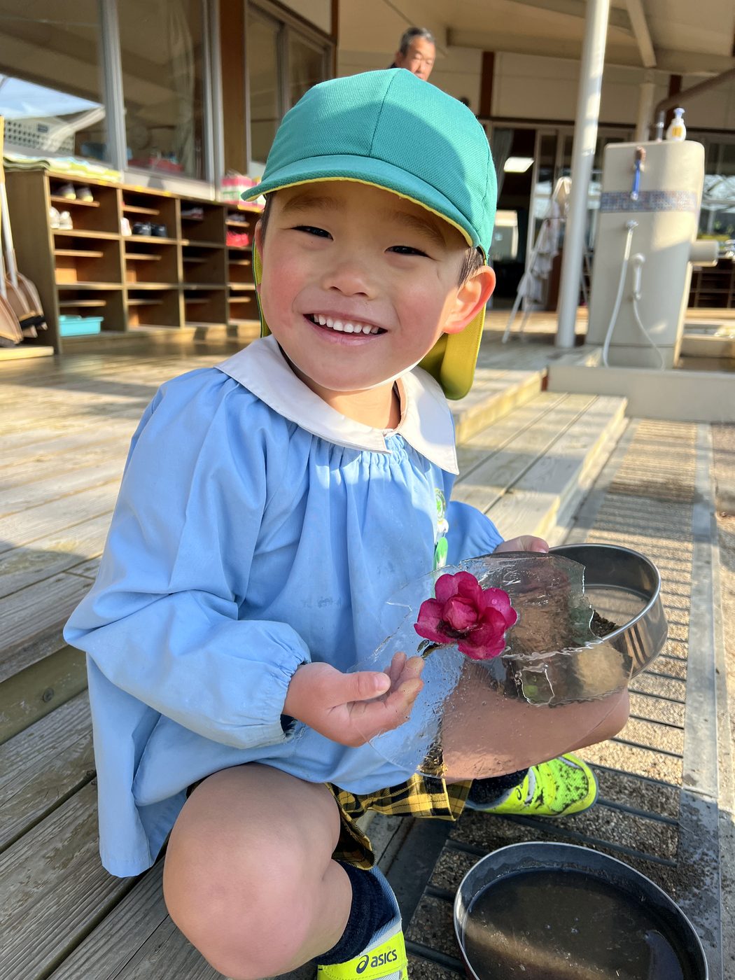 園のデッキで、小さな花を手に笑顔を見せる子ども